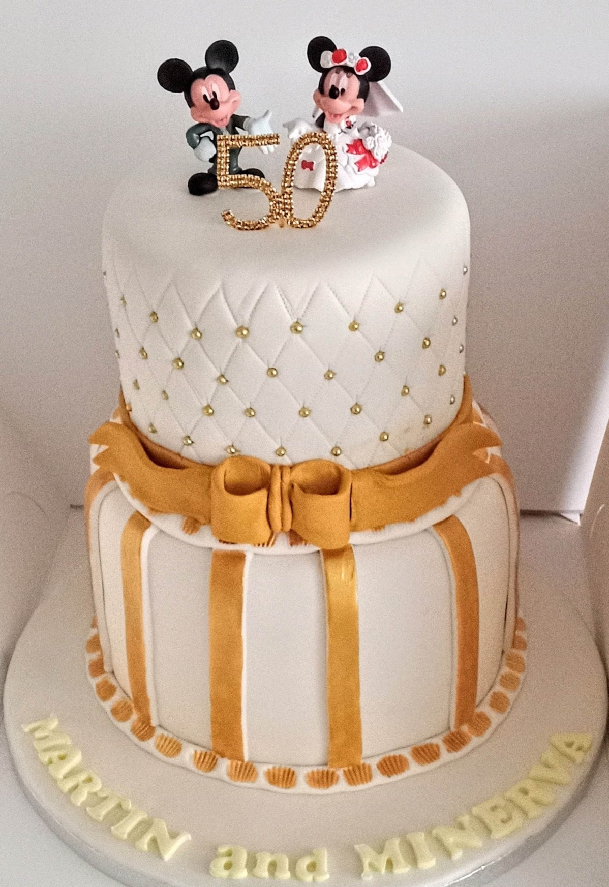 A 2 tier ivory and gold wedding cake with mickey bride and groom